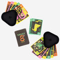 A vibrant "Tiger Tribe Crazy 8s + Go Fish Card Game Set" from TIGER TRIBE, featuring unique monster-themed illustrations on the cards, is spread out on a white surface. The deck is accompanied by two black, triangular cardholders, each holding several cards. The game's box is also visible.