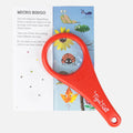 A red TIGER TRIBE Explorer Magnifying Glass rests on an open activity booklet. The page showcases colorful insects and plants with the heading "Micro Bingo." This nature exploration tool is ideal for kids' magnification, making those tiny illustrations come to life in vivid detail.