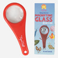 A red magnifying glass is displayed next to a colorful box adorned with illustrations of insects and a cheerful magnifying glass character. The box reads "TIGER TRIBE Explorer Magnifying Glass 2x 4x," "Handbook," and comes with an activity booklet for children’s nature exploration, all prominently featuring the TIGER TRIBE logo at the top.