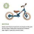 A white adjustable children's TryBike Steel from the brand TryBike, featuring beige tires and a brown seat. Above the bike is a small green badge with the number "2" on it. Below the bike, text explains that this 2-in-1 tricycle converts into a low balance bike, suitable for ages 2 to 6 years.