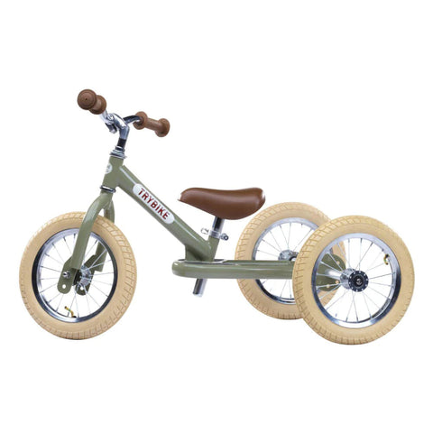 A TryBike Vintage Green 2-in-1 tricycle balance bike with beige tires and a brown seat. The TRYBIKE Steel frame supports two large back wheels and one front wheel. This model is perfect for learning to ride, featuring a silver handlebar with brown grips.