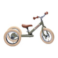 The TryBike - Vintage Green is a child's 2-in-1 tricycle balance bike designed for young riders learning to ride. It features a green frame with the word "TRYBIKE" in red letters, beige tires, brown handlebars, and a brown seat. The bike has two wheels at the back for added stability.