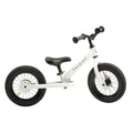 A white TryBike balance bike is shown, featuring black handlebars, a black seat, and black wheels. The minimalist design showcases the brand name "TryBike Steel" printed on the frame, emphasizing its 2-in-1 tricycle functionality.