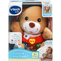 The image shows a boxed VTech Little Singing Puppy toy by Vtech. The packaging highlights features including 30+ sing-along songs, melodies, sounds, and phrases. It teaches first words and numbers with fun light-up buttons. The box indicates the loveable learning puppy is suitable for babies 3 months and older.