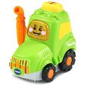 A VTech Toot-Toot Drivers Green Tractor featuring a smiling face on the front, with black wheels and orange hubs, and a yellow exhaust pipe on the side. The word "Tractor" is printed on the side of this toy that comes from VTech's Toot-Toot Drivers learning zone.