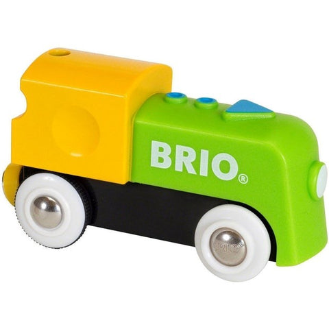 A brightly colored Brio My First Railway Battery Engine toy train with a yellow cab, green body, and black base. The word "Brio" is printed in white on the side. The children's toy features white wheels with silver centers and small blue and green buttons on top.