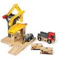 The Brio World Freight Goods Station from Brio is a colorful wooden toy set that includes a crane with a yellow, magnetic arm, a loading dock, a small cart, and a black and red truck. The set also comes with two small wooden cargo pieces featuring images of bananas. The Brio logo can be seen on multiple components of the set.