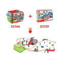 Image showing two boxed train toys labeled "HAPE Railway Bucket Builder Set" (E3764) and "HAPE Railway Bucket Builder Set" (E3729) with an arrow pointing down to an assembled train set. The 50-piece HAPE set includes a track, train cars, bridges, tunnels, trees, various characters and accessories to build your own town.