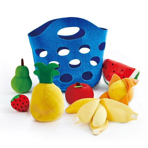 The HAPE Toddler Fruit Basket by HAPE features a blue felt basket with circular holes, surrounded by various colorful soft fabric fruits such as a pineapple, a banana, a red apple, a pear, a watermelon slice, and a strawberry. These adorable baby fruit toys are positioned in front of the soft felt basket.