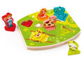 The Hape Farmyard Sound Puzzle, a colorful children's educational toy from the brand Hape, features various farm animals and a farmer. This engaging farm puzzle includes pieces like a cow, sheep, chicken, and horse, each fitting into uniquely shaped slots on a green board. The farmer stands next to the puzzle, not yet placed.