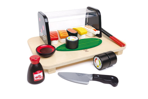 The HAPE Sushi Time by Hape features a wooden toy sushi set complete with a clear-topped display case, various detailed sushi pieces with colorful toppings, chopsticks, a soy sauce bottle, a play knife, two sushi rolls, and a green sushi mat.