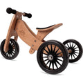 The Kinderboard Kinderfeet Tiny Tot Plus - Bamboo is a wooden balance tricycle featuring three black spoked wheels, black rubber handlebars, and a curved wooden seat. Showcasing a natural bamboo finish with black accents, this 2-in-1 bike is designed to help young children effortlessly transition from tricycle to balance bike.