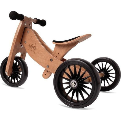 The Kinderboard Kinderfeet Tiny Tot Plus - Bamboo is a wooden balance tricycle featuring three black spoked wheels, black rubber handlebars, and a curved wooden seat. Showcasing a natural bamboo finish with black accents, this 2-in-1 bike is designed to help young children effortlessly transition from tricycle to balance bike.