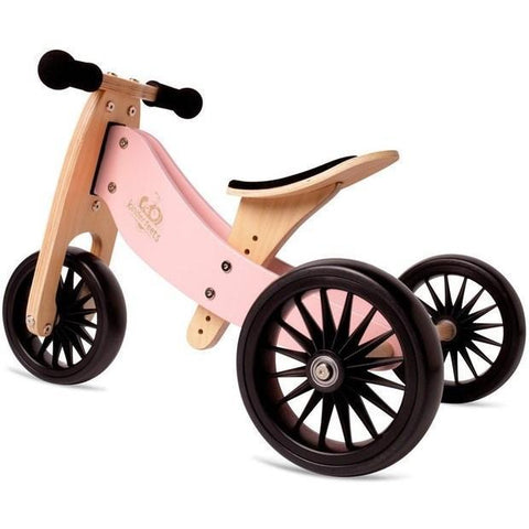 A Kinderboard Tiny Tot Plus - Rose, this small wooden tricycle features a pink frame, black handlebars, and black wheels. The seat combines a natural wood finish with black accents. With its three large spoked wheels and minimalist design, this 2-in-1 bike offers style and versatility.