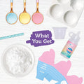 Flat lay of Klutz Make Your Own Bath Bombs Scented Bakery kit materials, including colored powders on spoons, a mold, a small cup, a pink liquid bottle, baking soda on a plate, a striped straw, and cut-out packaging parts. All items are ready to be assembled into your perfect gift box. Text in the center reads "What You Get.