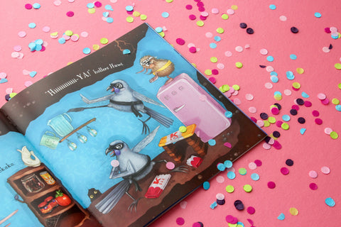 An open copy of "Kuwi's Rowdy Crowd" by Kat Merewether, from the KUWI THE KIWI brand, lies on a pink surface sprinkled with colorful confetti. The illustration depicts two birds and a cat with glasses in a kitchen filled with household items and a pink refrigerator, accompanied by visible dialog text.