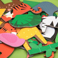 A pile of colorful, cartoon-like animal-shaped puzzle pieces from the MIEREDU Magnetic Art Case - Animal World by MIEREDU are scattered on a green surface. This educational magnetic game includes parts of a tiger, elephant, zebra, crocodile, and other animals, characterized by bright colors and simplified features to stimulate a child's imagination using eco-friendly materials.