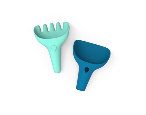 The image showcases two vibrant, open-ended toys for children: a mint-green rake with four prongs and a dark blue scoop. Designed by QUUT, these tools are perfect for sand play or as children's garden instruments. The QUUT Raki Rake & Digger in pink is especially suited for versatile travel games at the beach or backyard adventures.