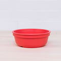 A REPLAY Re-Play Bowl, distinguished by its round, red design and slightly raised sides, rests on a light wooden surface. The backdrop is a clean white tiled wall. This colorful piece of tableware is crafted from recycled plastic bowls, ensuring it is both safe and suitable for kids.