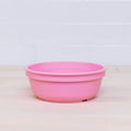 A vibrant pink Re-Play Bowl from REPLAY's colorful tableware set is placed on a light wooden surface with a white tiled wall in the background. Made from recycled plastic, the bowl is empty and features a simple, smooth design that is safe for kids.