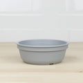 A Re-Play Bowl from REPLAY, made of gray recycled plastic, is placed on a light wood surface. The background consists of white tiled walls. The bowl has a simple, unadorned design, ideal and safe for kids.