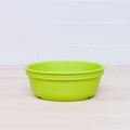 A vibrant Re-Play Bowl from REPLAY, in bright green, sits on a light wooden surface. The background showcases glossy, white tiled walls. Crafted from recycled plastic, this shallow round bowl is also safe for kids.