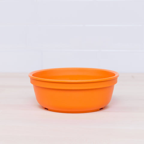 A Re-Play Bowl from REPLAY's vibrant tableware set sits empty on a light wooden surface with a white tiled wall in the background, showcasing its recycled plastic design that's safe for kids.