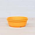 A Re-Play Bowl by REPLAY, crafted from recycled vibrant orange plastic with a round shape and slightly flared rim, is placed on a light wooden surface. Safe for kids, it seamlessly blends into any home with its cheerful design against the white tiled background.