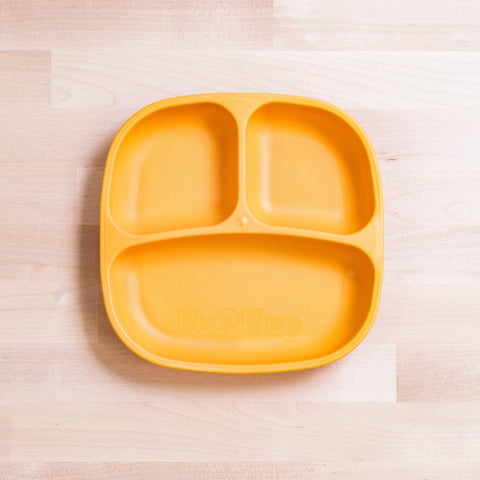 A yellow Re-Play Divided Plate from REPLAY, made from recycled plastic, features three compartments arranged in a smiley face pattern. It's placed on a light wood surface and has "Re-Play" embossed at the bottom of the largest compartment, making it ideal for toddlers and portion control.