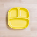 A yellow Re-Play Divided Plate from REPLAY, made of recycled plastic with a rectangular shape and rounded edges, features three compartments for separating different types of food and is placed on a light wooden surface.