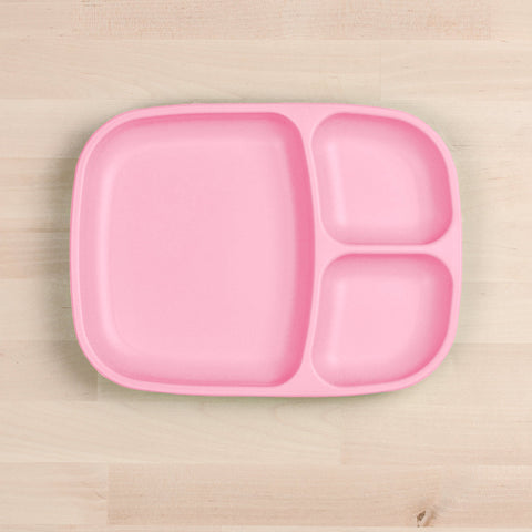 The REPLAY Re-Play Divided Tray is a durable, pink rectangular plate made from recycled material with rounded edges. It features three separate compartments: one large section on the left and two smaller sections on the right, all positioned on a light wood surface.