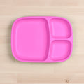 A bright pink, eco-friendly Re-Play Divided Tray made from recycled material sits on a light wooden surface. The REPLAY tray features a compartmentalized design with three sections: one large section on the left and two smaller sections stacked on the right. This durable tableware is rectangular with rounded edges.