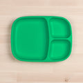 The REPLAY Re-Play Divided Tray, an eco-friendly green plate with three compartments, is placed on a light wooden surface. Made of recycled material, this durable tableware features one large section on the left and two smaller sections stacked on the right.