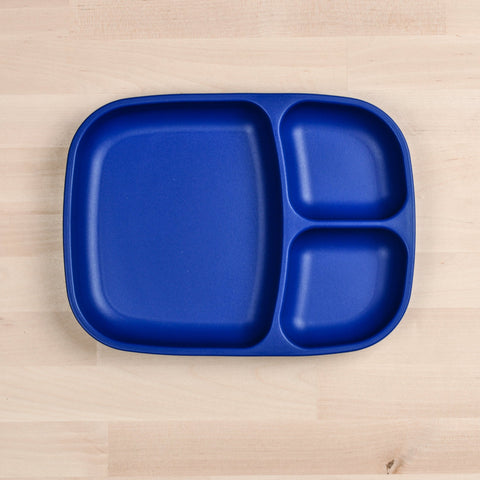 A blue, rectangular Re-Play Divided Tray from REPLAY, featuring three compartments, sits on a light wood surface. Crafted from durable, recycled material, the tray includes one large section on the left and two smaller sections on the right, making it an eco-friendly choice for any meal.