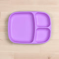 The Re-Play Divided Tray from REPLAY, a purple, three-compartment rectangular plate made from recycled materials, is set on a light wooden surface. The largest compartment is on the left, and the two smaller compartments are on the right, one above the other. This piece of durable tableware is both practical and eco-friendly.
