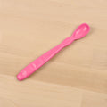 A Re-Play Infant Spoon by REPLAY, featuring a pink plastic design with a long handle and rounded tip, lies on a light wooden surface. The handle includes small round indents for grip and has the word "Bébé" embossed on it. Made from recycled materials, this sustainable tableware ensures both safety and eco-friendliness.