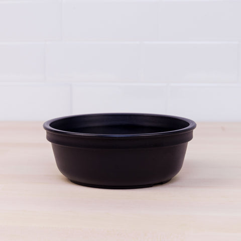 A REPLAY Re-Play Large Bowl, made from black recycled plastic with a wide rim and round shape, sits on a light-colored wooden surface. The background features white subway tiles.