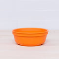 A Re-Play Large Bowl by REPLAY, made from orange BPA-free plastic, rests on a light wooden surface with a white tiled wall in the background.