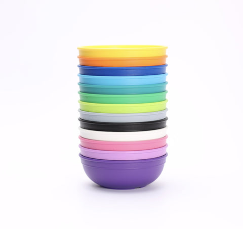 A stack of REPLAY Re-Play Large Bowls, made from BPA-free recycled plastic, arranged neatly on a white background. The bowls come in a variety of colors including yellow, blue, green, purple, pink, and black, creating a bright and vibrant composition.