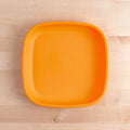 An overhead view of the Re-Play Large Flat Plate by REPLAY, a square orange plate made in America from recycled plastic dinnerware, placed on a light wooden surface. The plate features rounded corners and is empty.