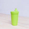 The REPLAY Re-Play No-Spill Sippy Cup, made from FDA approved recycled green plastic and featuring a convenient spout lid, sits on a light wooden surface with a white tiled wall in the background.