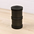 A cylindrical, black Re-Play Snack Stack from REPLAY features indented grooves and the text "Red Play" embossed on it. Made from recycled material, this durable snack container is segmented into three parts and sits on a light wooden surface in front of a white tiled wall.