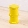 A large, yellow cylindrical container with ribbed edges, resembling stacked rings or sections. Made of recycled material, the durable REPLAY Re-Play Snack Stack is placed on a light wood surface with a white tile wall in the background.