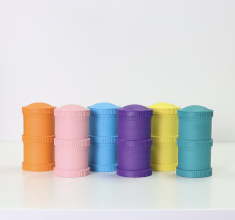 Re-Play Snack Stacks from REPLAY, made from recycled materials, are lined up in a row on a white surface. These durable cylindrical containers come in six distinct colors: orange, pink, blue, purple, yellow, and teal. Each container features a ribbed texture and a rounded top.