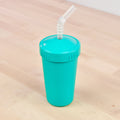 A Re-Play Straw Cup by REPLAY, featuring a vibrant turquoise color and made from durable plastic, complete with a matching lid and an integrated flexible, translucent straw, shown resting on a light wooden surface.