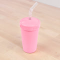 The REPLAY Re-Play Straw Cup, a pink plastic cup made in the USA, comes with a matching screw-on lid and a flexible, clear straw. Ideal for cold drinks, this sustainable design features a textured grip around the top and is displayed elegantly on a light wooden surface.