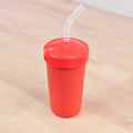 A red REPLAY Re-Play Straw Cup with a matching lid and a flexible, partially bent straw is placed on a light wooden surface. Made in the USA, the cup features a textured grip, and the straw—crafted from recycled materials—enhances its eco-friendly design.