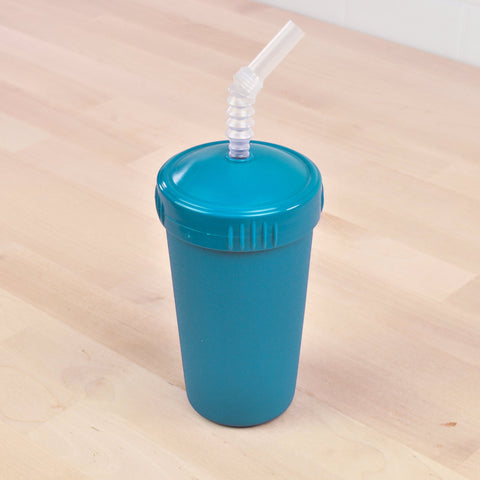 A Re-Play Straw Cup by REPLAY, designed in sustainable blue and equipped with a flexible, clear plastic straw, stands on a light wooden surface. Made in the USA, the tumbler features a fitted lid that secures the straw in place.