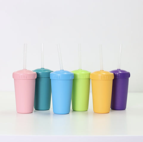 Six REPLAY Re-Play Straw Cups with matching lids and translucent straws are arranged in a row on a white surface. The cups come in light pink, teal, light blue, lime green, yellow, and purple. Made in the USA, they sit against a plain white wall.