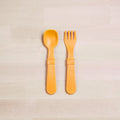 A pair of orange Re-Play Utensil Set from REPLAY is placed on a light wooden surface. The set includes a spoon and a fork, each with wide handles and rounded edges, designed for easy grip and safe use by young children. Made from recycled plastic, these utensils are also dishwasher safe.